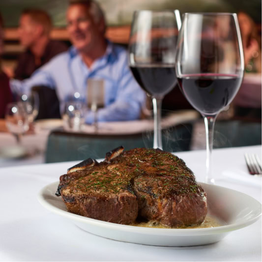 Juicy Ruth's Chris steak with two glasses of red wine at an elegant restaurant table.