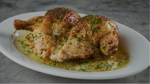 Juicy roasted chicken drizzled with savory herb sauce on a white plate at Ruth's Chris Steak House.