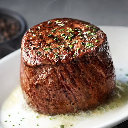 Juicy, perfectly cooked filet mignon steak garnished with herbs, served with butter sauce for an upscale dining experience at Ruth's Chris.