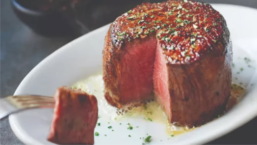 Juicy, perfectly cooked medium-rare filet mignon steak served with herb butter, showcasing Ruth's Chris signature steakhouse quality and premium beef selection.
