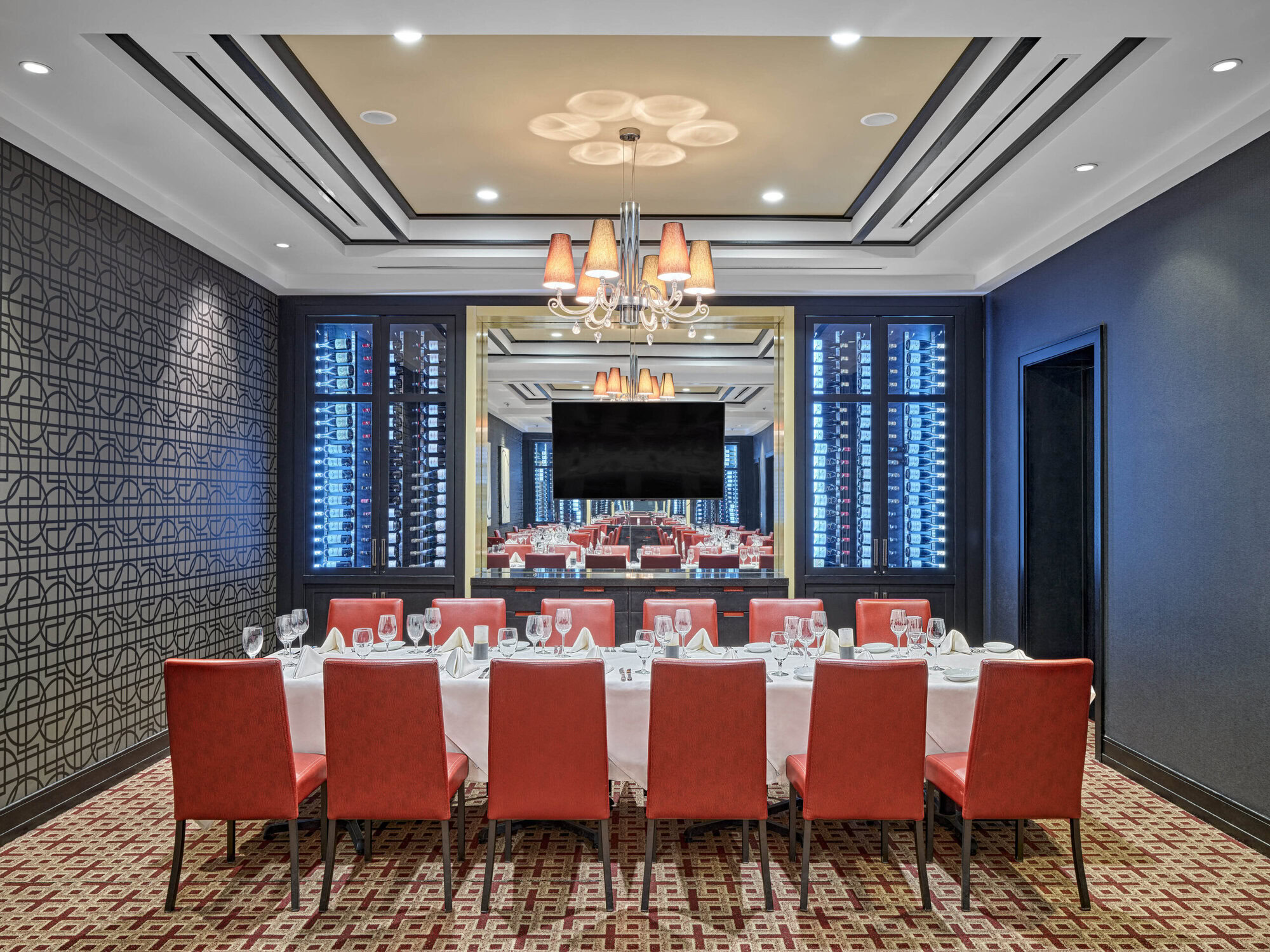 Elegant fine dining restaurant interior with a spacious table setting, plush red chairs, sophisticated lighting, and a large wine display, exemplifying upscale American steakhouse ambiance at Ruth's Chris.